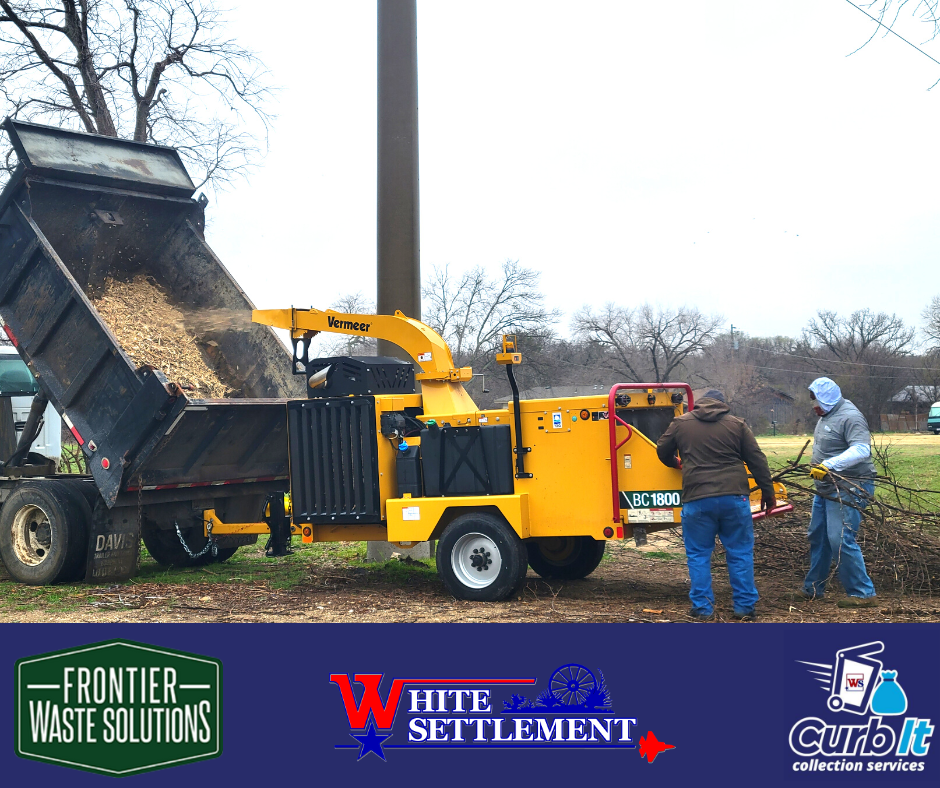 two workers put tree limbs into a wood chipper